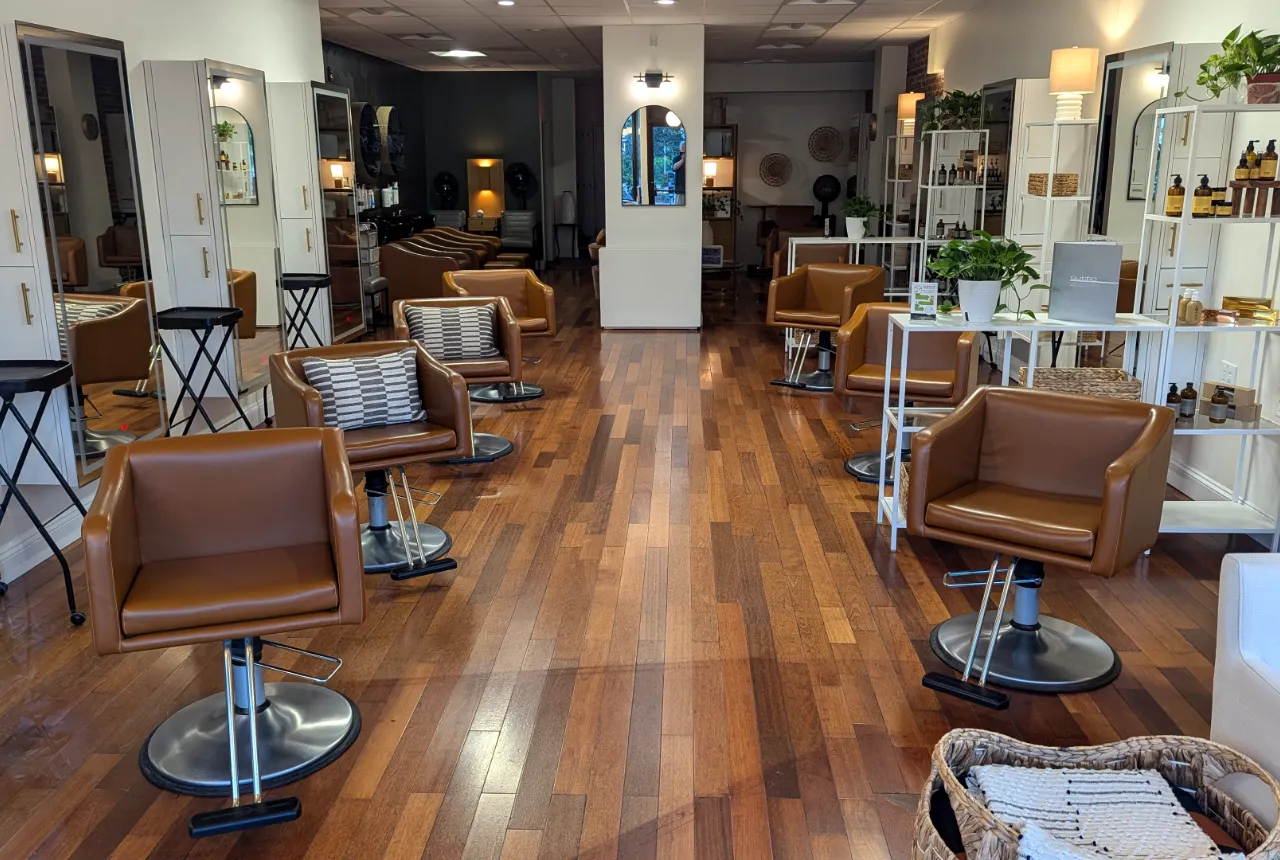Sfeerbeeld van een kapsalon met houten vloer, spiegels en lege stoelen.